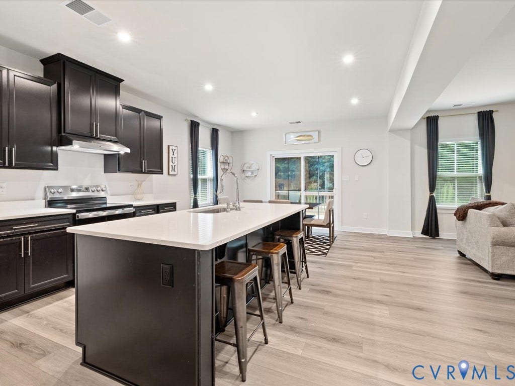Open-concept kitchen featuring dark wood-finish cabinetry, white countertops, stainless steel appliances, and a central island with a sink