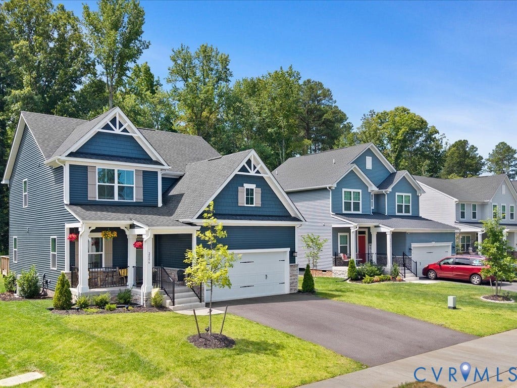 Siding exterior with dormer accents, covered porch, attached garage, and paved driveway