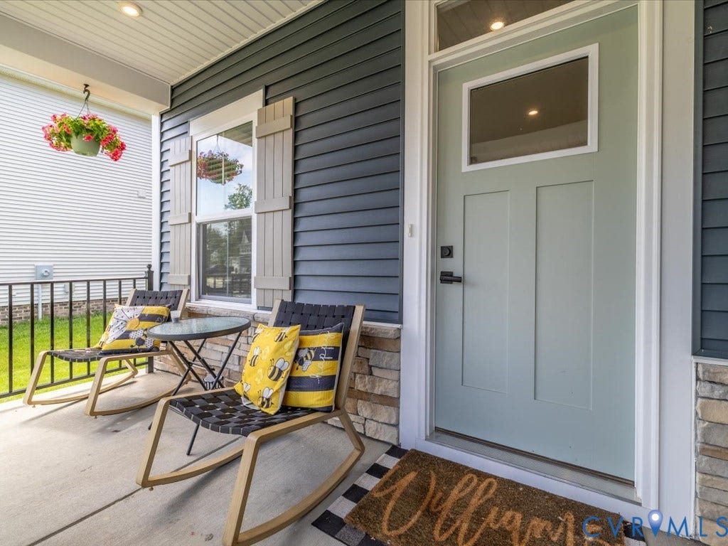 Covered front porch featuring dark blue siding, stone veneer accents, and a light green paneled front door with an upper glass insert