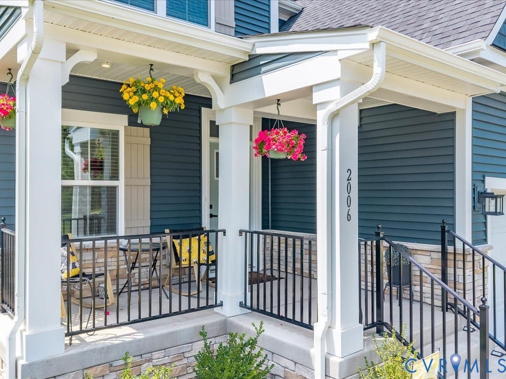 Covered porch with white columns, stone veneer accents, dark siding, and black iron railings