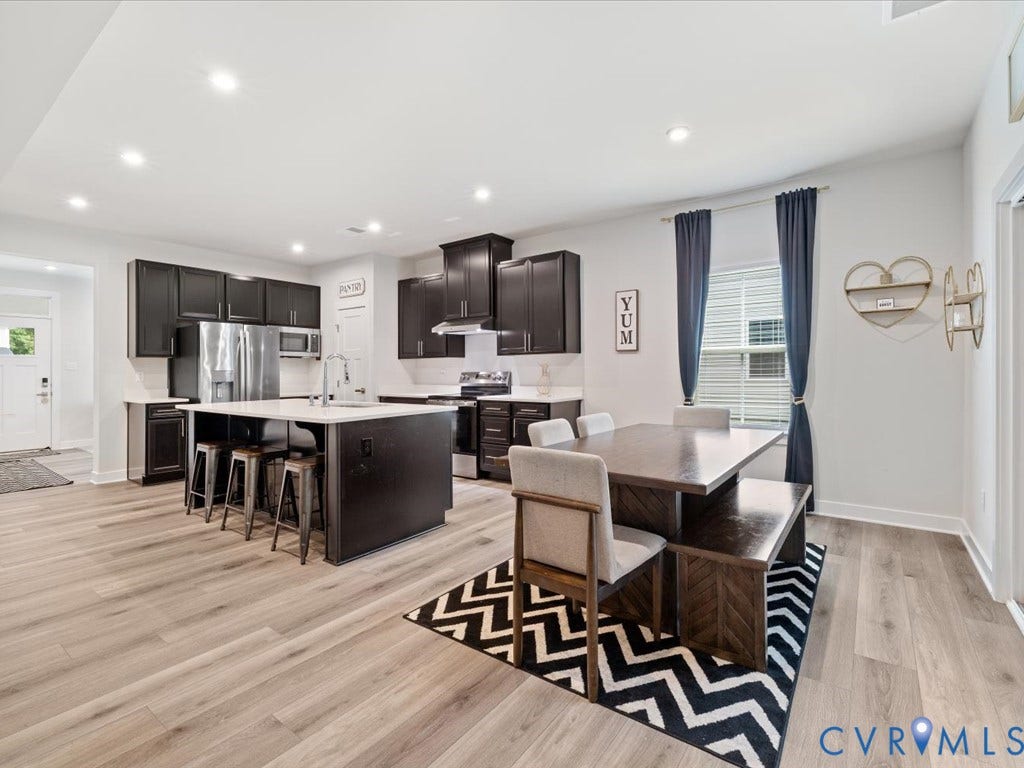 Open-concept kitchen featuring dark cabinetry, stainless steel appliances, a center island with countertop seating, and light-tone wood-finish flooring