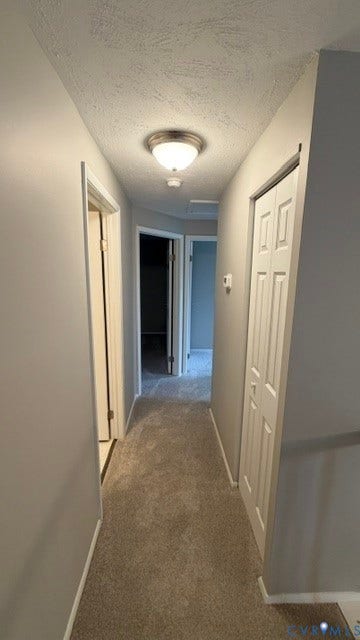 Hallway featuring gray wall paint, textured ceiling, flush-mount lighting, gray carpet flooring, and paneled bifold doors