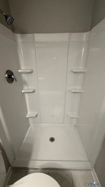 White shower surround with integrated shelving, chrome fixtures, and a ceiling-mounted shower head
