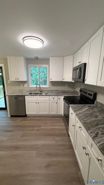 White cabinetry, gray patterned countertops, stainless steel appliances, wood-finish flooring, and a sliding glass door