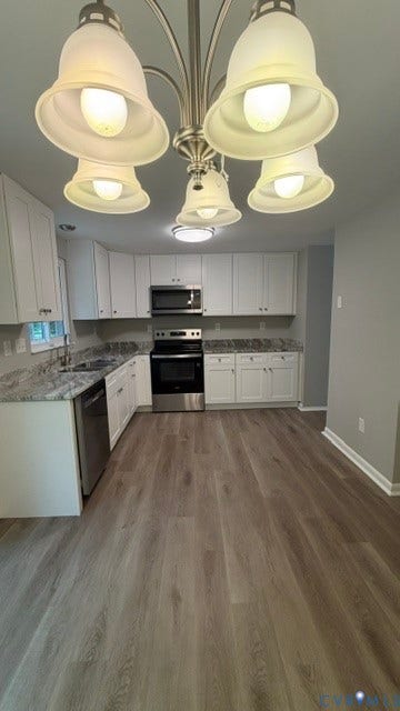 Updated kitchen featuring white shaker cabinetry, stainless steel appliances, light-toned wood-finish flooring, and a multi-light chandelier