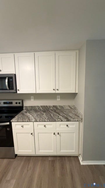 White cabinetry, gray patterned countertops, stainless steel appliances, wood-finish flooring, and a sliding glass door