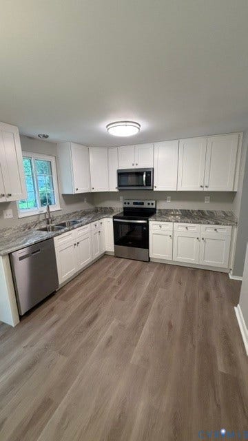 Kitchen featuring white cabinetry, stone countertops, wood-finish flooring, stainless steel appliances, and an undermount sink
