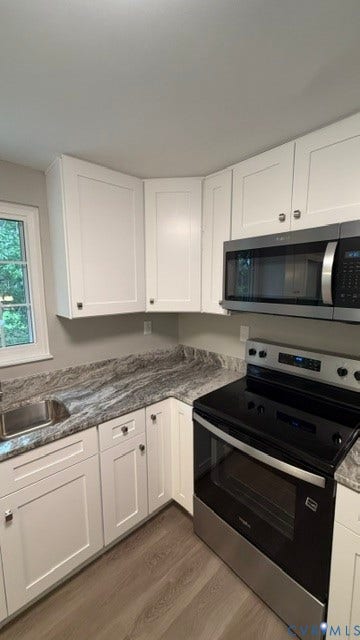 Updated kitchen featuring white shaker-style cabinetry, a stainless steel sink, wood-finish flooring, and a stainless steel oven with an above-range microwave