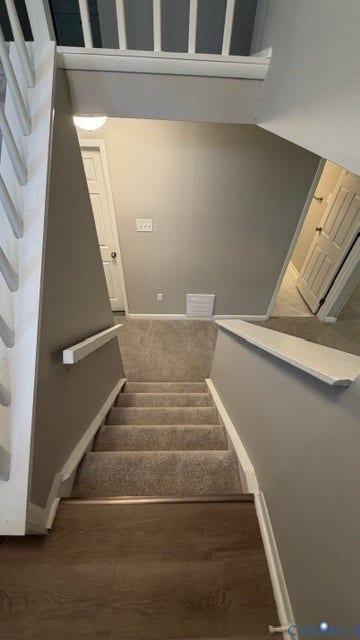 Staircase featuring wood-finish flooring transitioning to carpeted steps, white painted handrails, and neutral wall paint