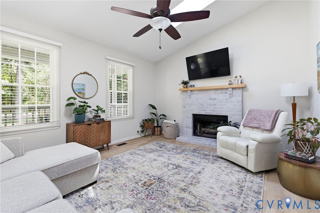 10744 Brookley Road, Glen Allen, VA 23060 Vaulted ceiling with a ceiling fan, light wood-finish flooring, white brick fireplace with a wood mantel, and multiple windows