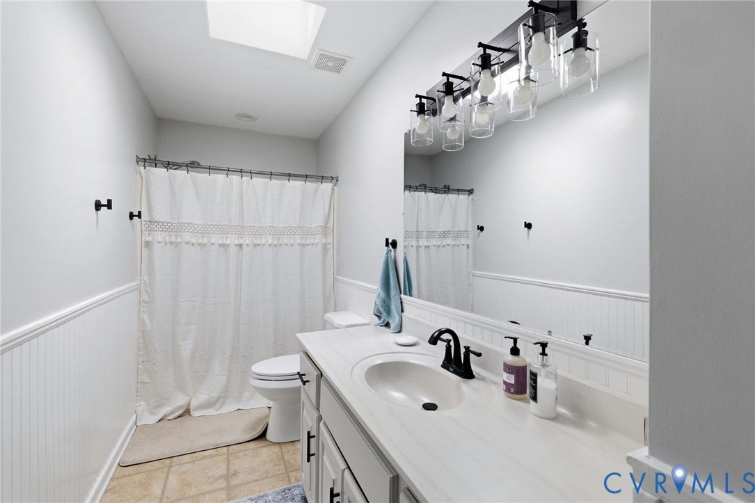 10744 Brookley Road, Glen Allen, VA 23060 Bathroom featuring a single vanity with a white countertop, an integrated sink with a matte black faucet, and a large mirror with a multi-bulb light fixture