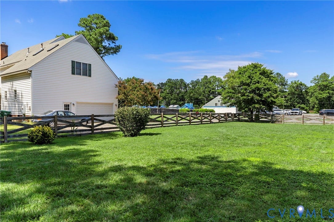 10744 Brookley Road, Glen Allen, VA 23060 White siding exterior with a side-entry garage, gabled roofline, and a split-rail fence enclosing a manicured lawn