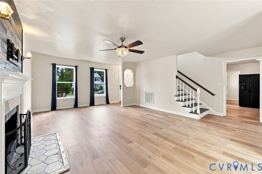 2807 Executive Drive, John Tyler Woods, Chesterfield, VA 23831 Light wood-finish flooring, a ceiling fan with integrated lighting, a fireplace with a white mantel and hexagonal tile hearth, and a staircase with white risers and a dark wood handrail