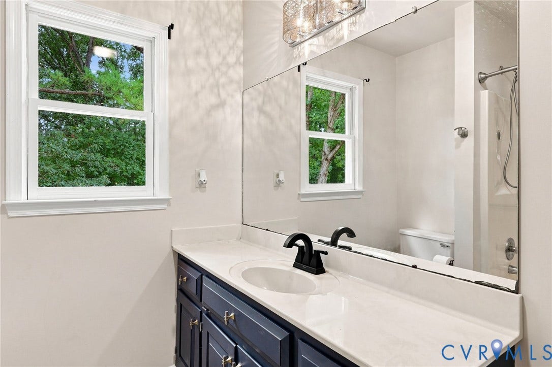 2807 Executive Drive, John Tyler Woods, Chesterfield, VA 23831 White single-hung window, full-width vanity mirror, dark blue wood-finish vanity, white countertop with integrated sink, and black finish faucet