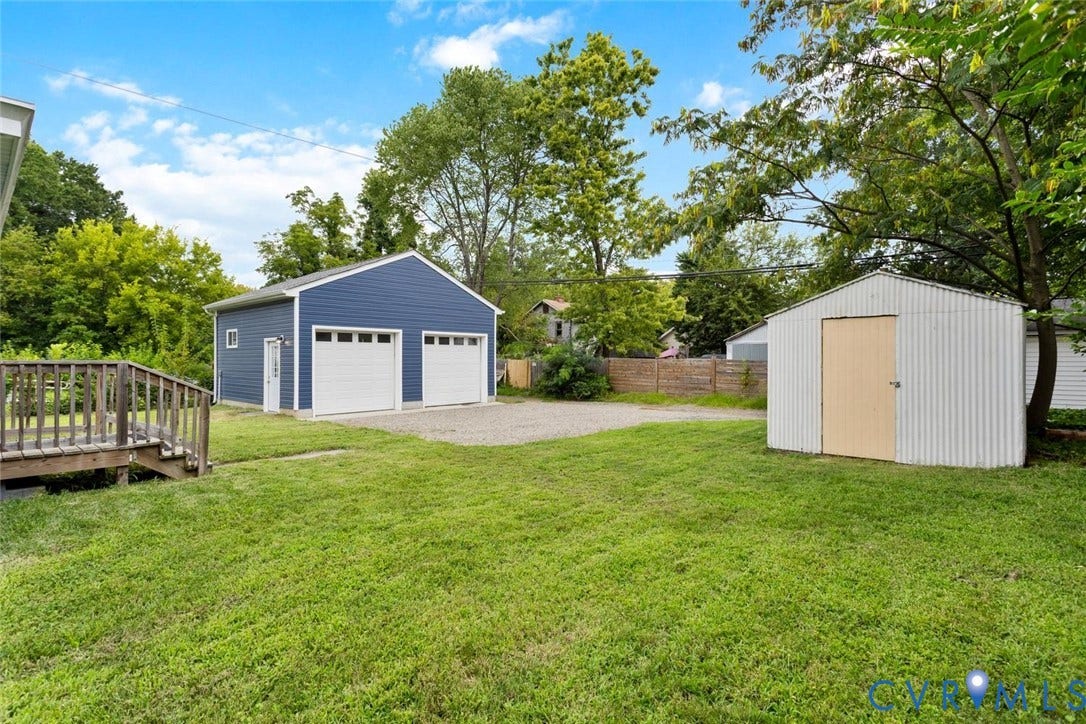 Expansive grassy yard featuring a detached two-car garage, gravel driveway, and a separate storage shed
