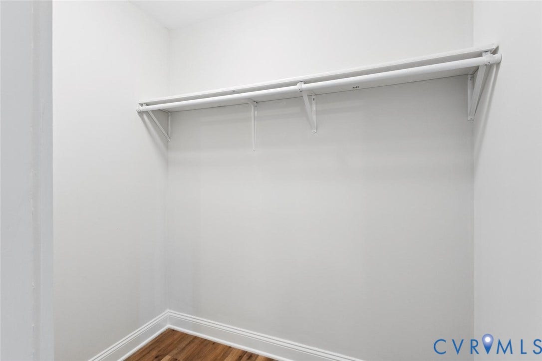 Closet featuring wall-mounted shelving, dual hanging rods, and wood-finish flooring