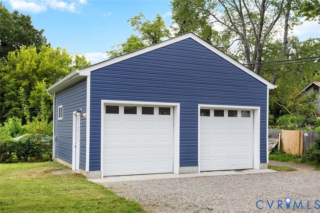Detached two-car garage with blue horizontal siding, white trim, and two paneled garage doors with upper windows