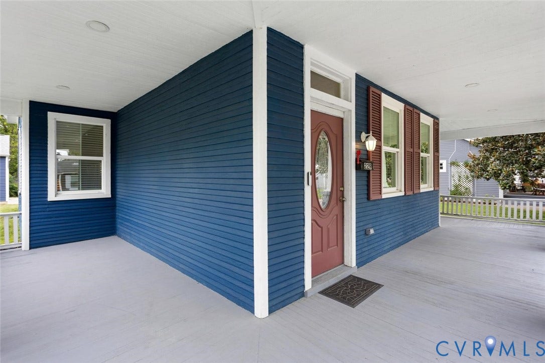Covered front porch with blue horizontal siding, white trim, red entry door, and brown louvered shutters