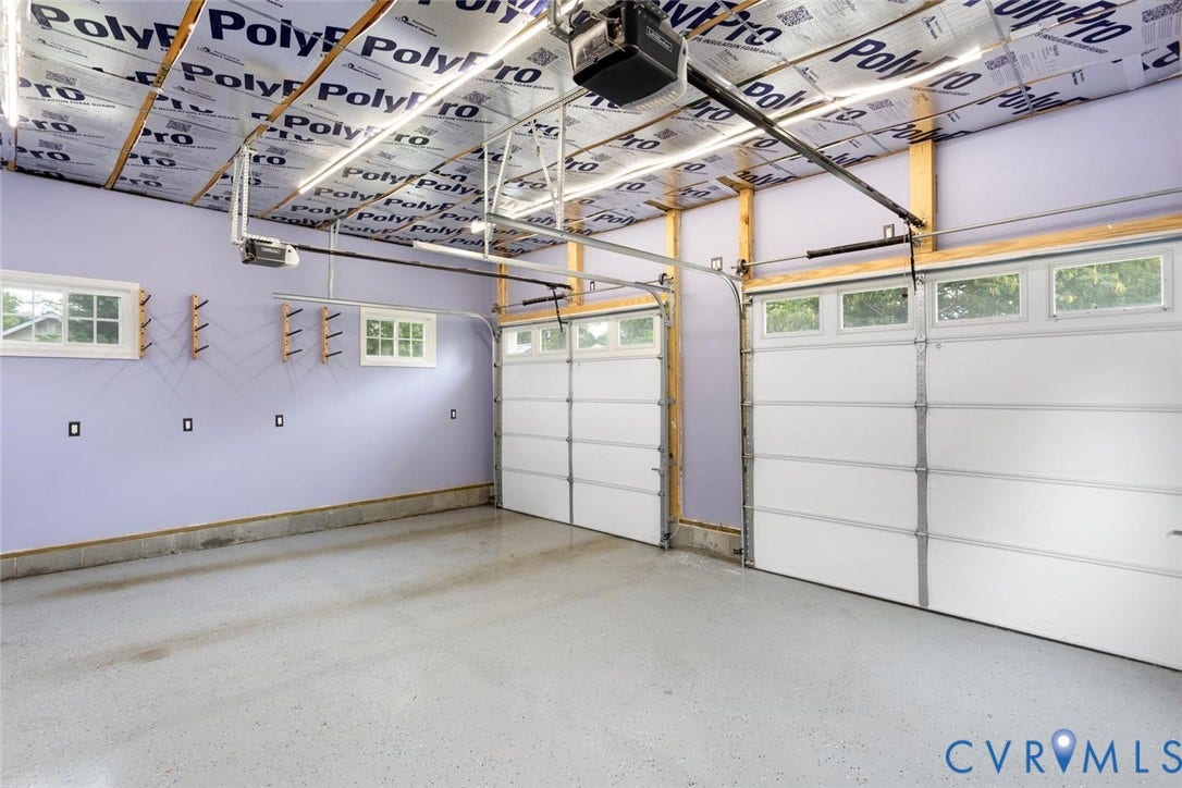 Two overhead garage doors with window panels, multiple windows, and a finished concrete floor