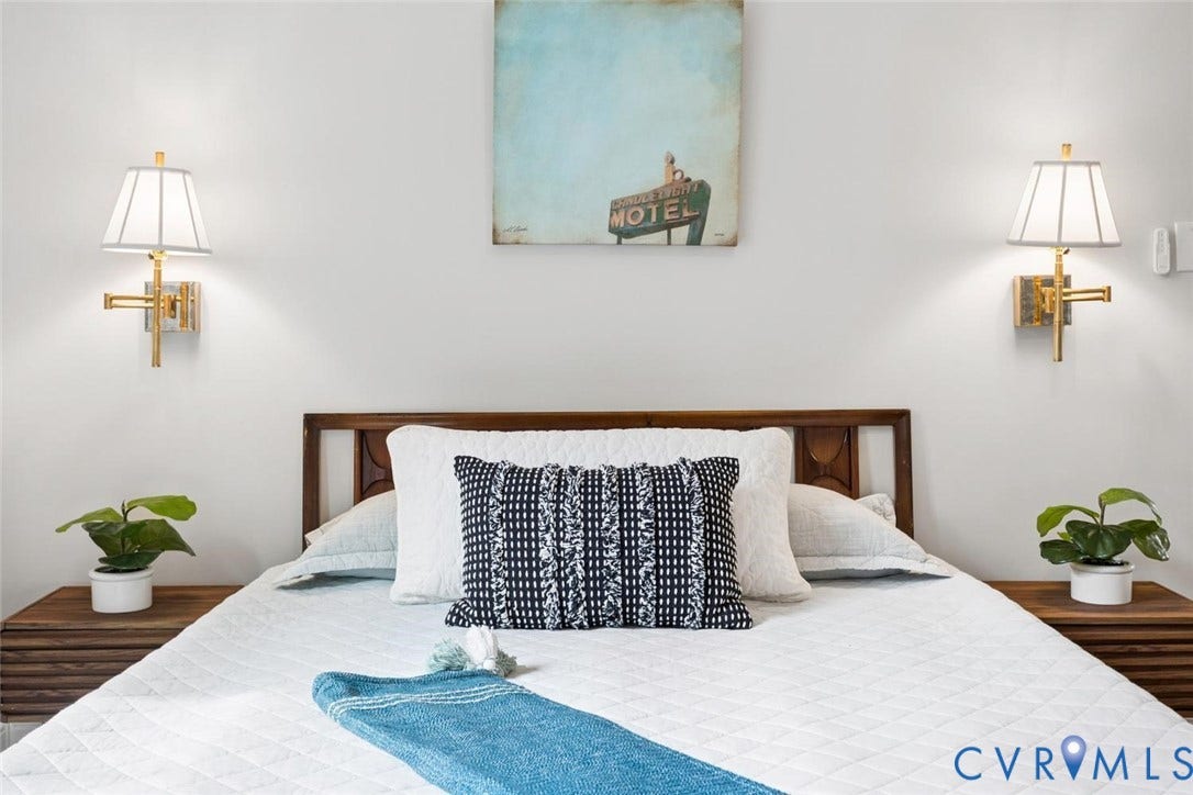 White wall finish, symmetrical gold-tone wall sconces with pleated shades, wood headboard, and wood-finish bedside tables
