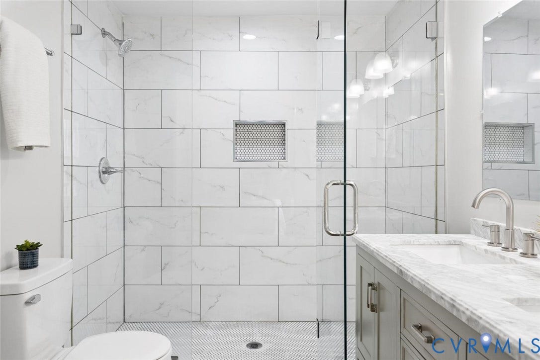Glass-enclosed shower with white tiled walls and perforated shower niche
