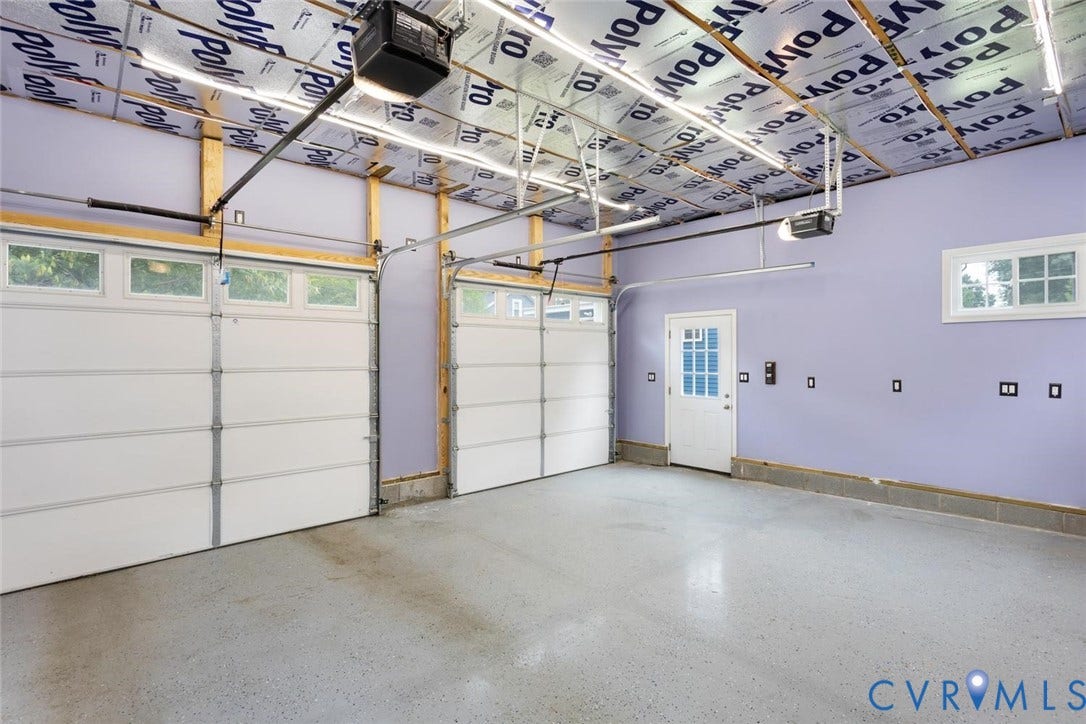 Two overhead garage doors with window inserts, an additional entry door with window panes, two casement windows, exposed ceiling joists, and a finished floor surface