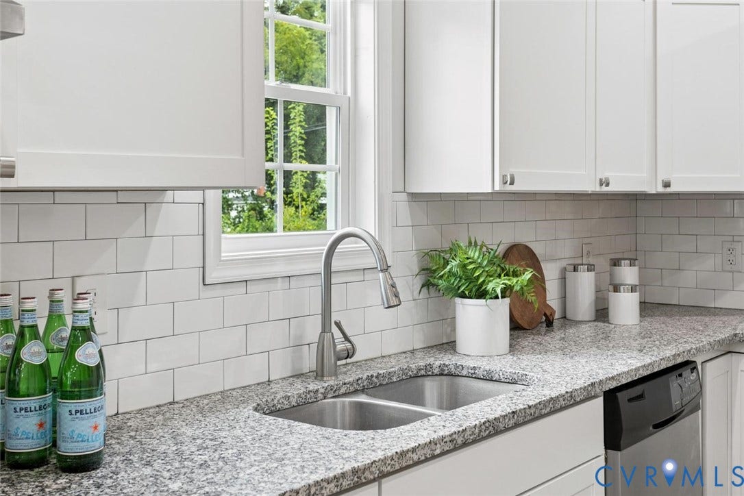 White shaker cabinetry, speckled countertops, stainless steel dual basin sink, subway tile backsplash, and a built-in dishwasher