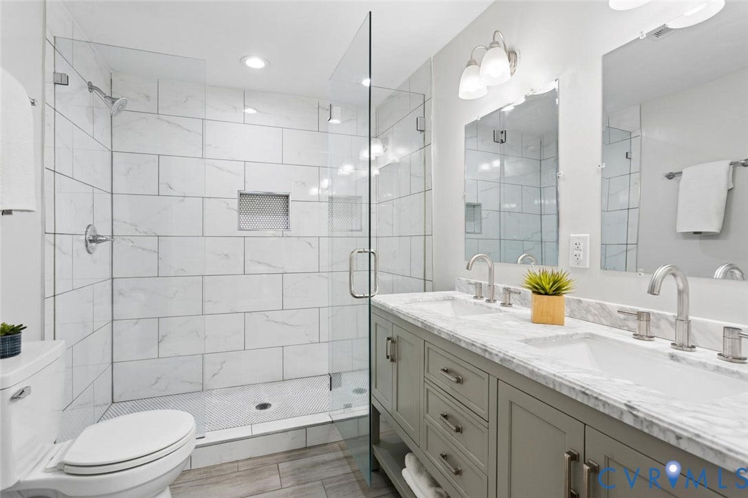 Glass-enclosed shower with subway tile and integrated niche, dual vanity with undermount sinks, stone countertops, and brushed nickel fixtures
