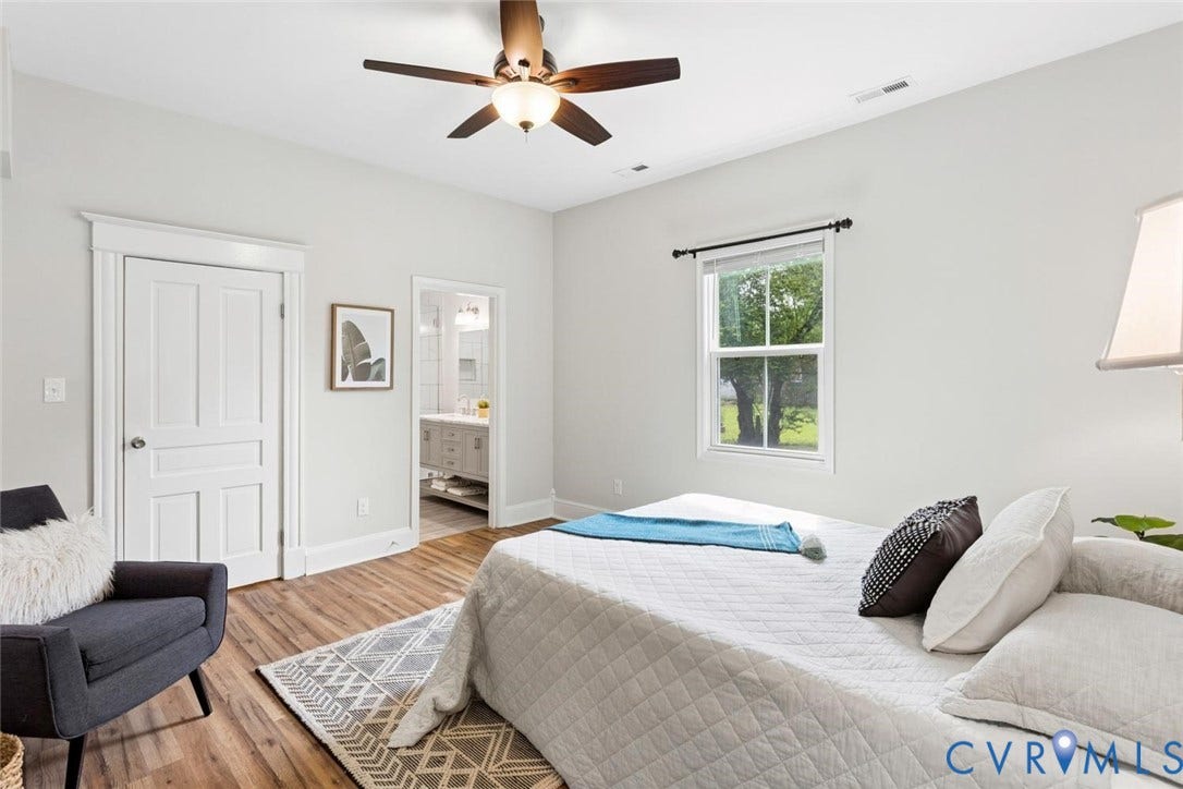 Wood-finish flooring, ceiling fan, white paneled doors with trim, double-hung window, and a visible bathroom with a vanity