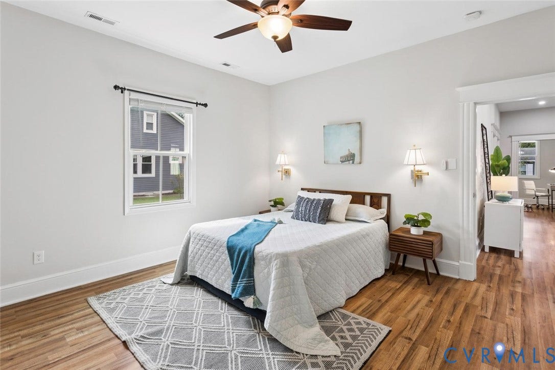 Wood-finish flooring throughout, ceiling fan with integrated lighting, recessed window with white trim, and a wide cased opening to an additional space