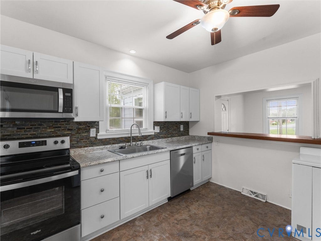 Kitchen featuring white cabinetry, stainless steel appliances, granite-style countertops, mosaic tile backsplash, and a pass-through window with a wood-finish bar top