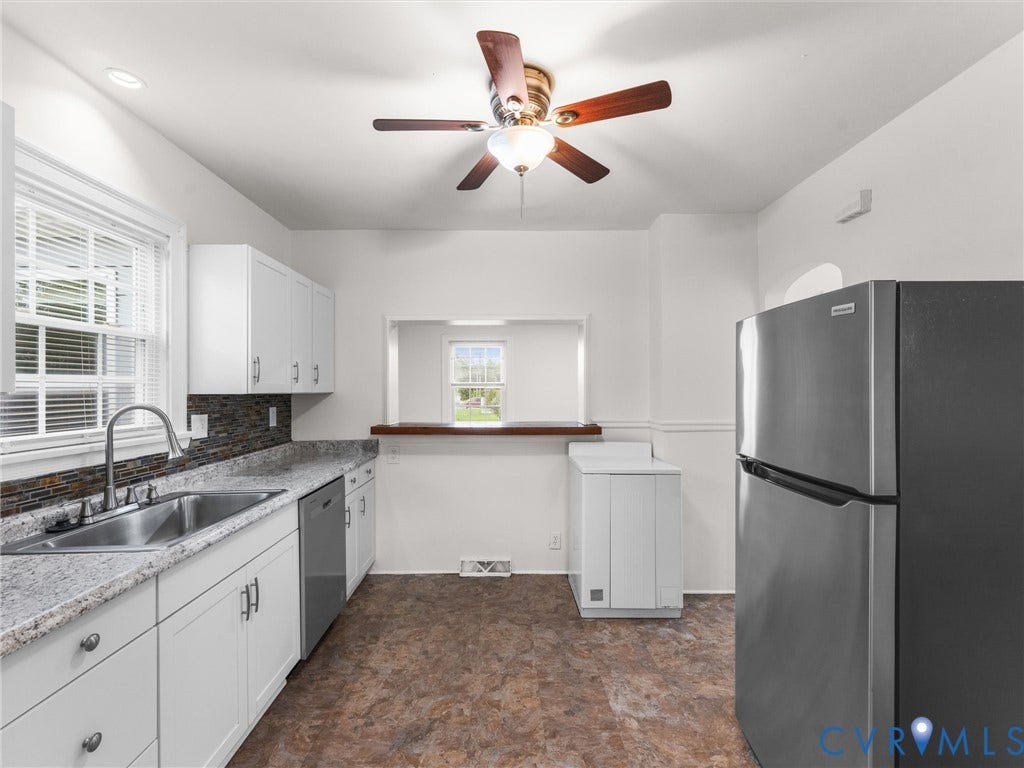 Kitchen featuring white cabinetry, light-toned countertops, a stainless steel sink, and a multi-toned backsplash