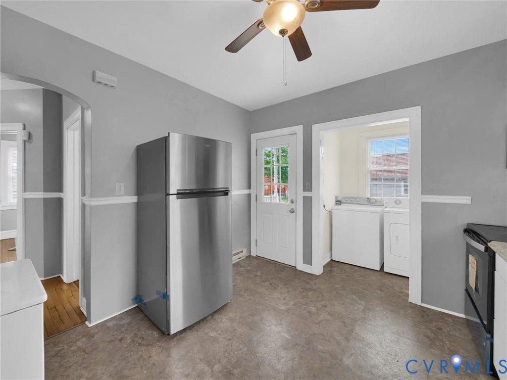 Kitchen area featuring a stainless steel refrigerator, neutral gray walls with white wainscoting, and durable flooring
