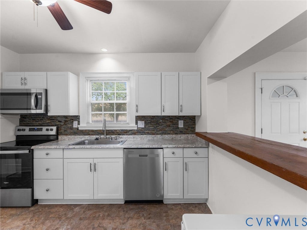 Modern kitchen featuring white shaker cabinetry, stainless steel appliances, a multi-tone tile backsplash, and a light-toned countertop