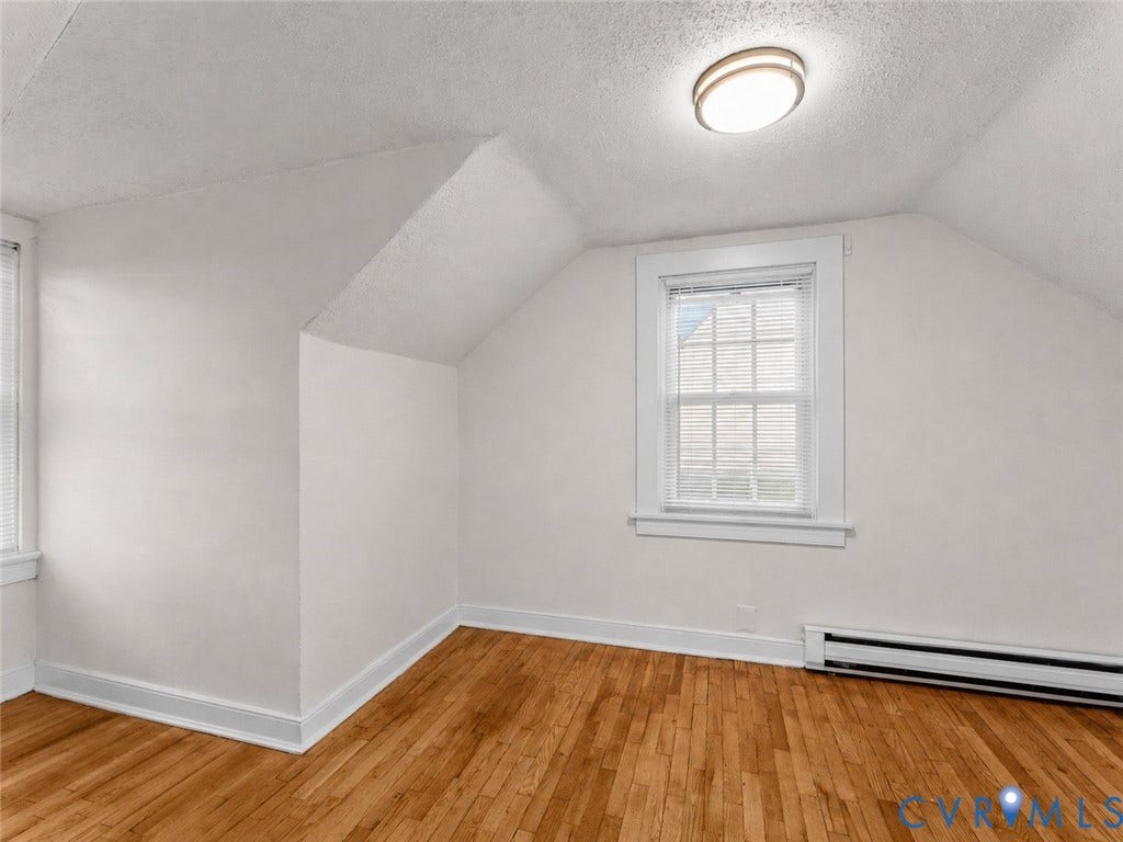 Room featuring hardwood flooring, sloped ceiling, window with white blinds, baseboard trim, and a flush-mount ceiling light