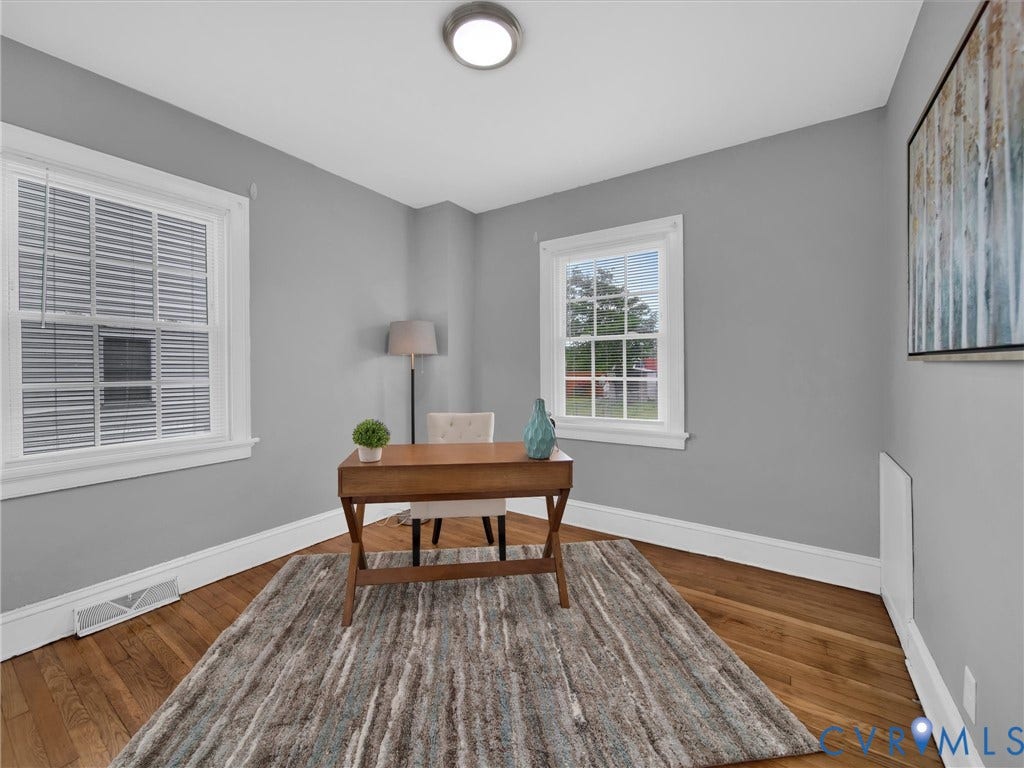Hardwood flooring with a decorative area rug, two windows with white trim, and light gray wall paint