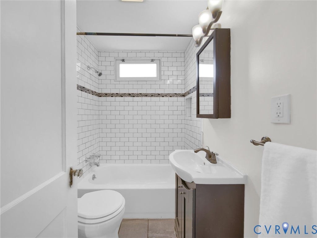 Bathroom featuring a white subway tile shower surround with a decorative accent band, a white bathtub, and a window within the shower enclosure