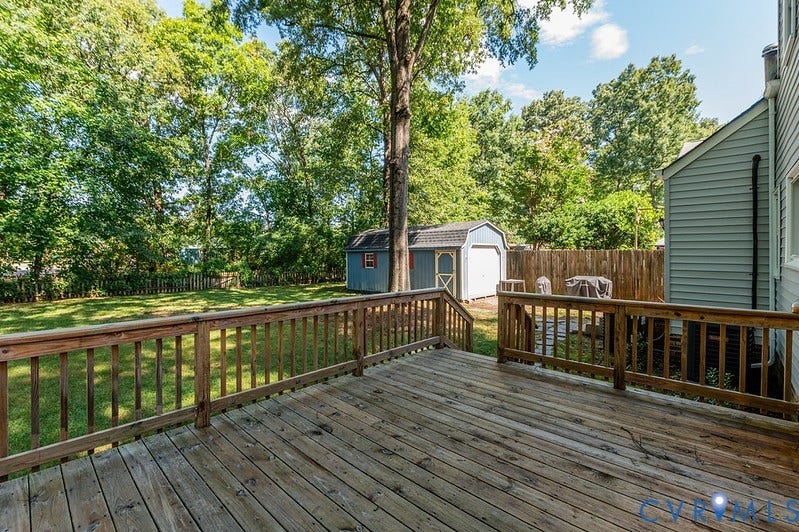 2016 Wrens Nest Road, Settlers Landing, Richmond, VA 23235 Expansive wood deck with railing, leading to a green lawn with a wooden privacy fence and two storage sheds