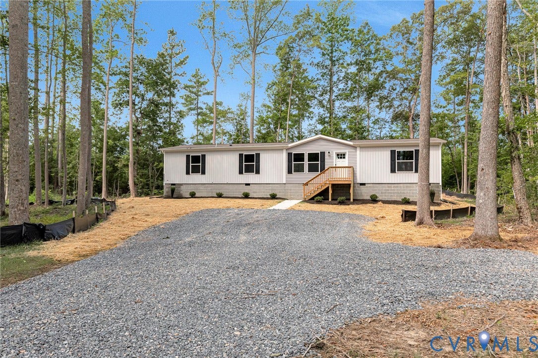 15263 Cross County Road, Mineral, VA 23117 White exterior siding, black window shutters, wood-finish front porch steps, gravel driveway, and surrounding mature trees