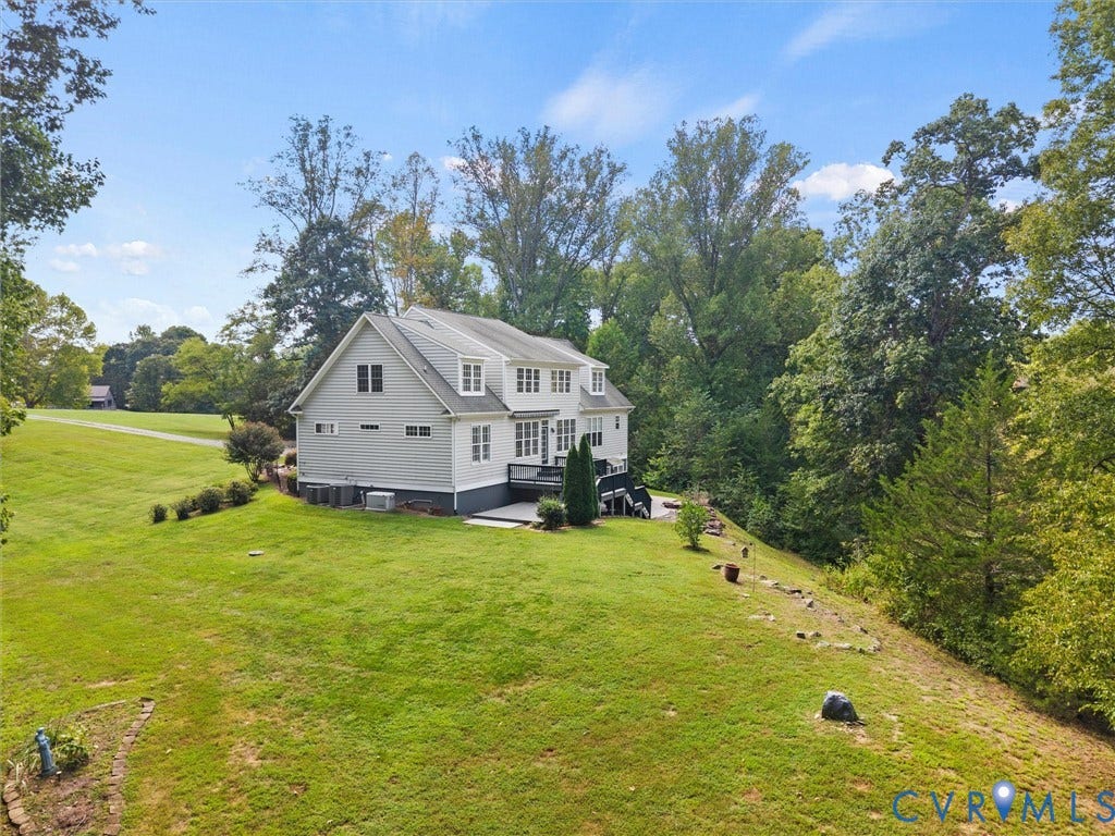 6126 Cartersville Road, Powhatan, VA 23139 Exterior featuring light-colored siding, multiple windows, a dark-colored deck, and a sloping grassy yard bordered by mature trees