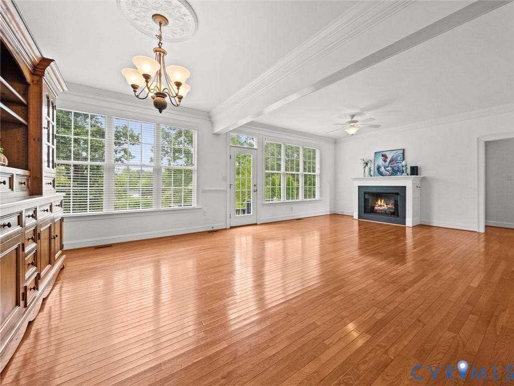 6126 Cartersville Road, Powhatan, VA 23139 Hardwood flooring throughout, featuring a fireplace with a white mantel, multiple large windows, and a built-in display cabinet