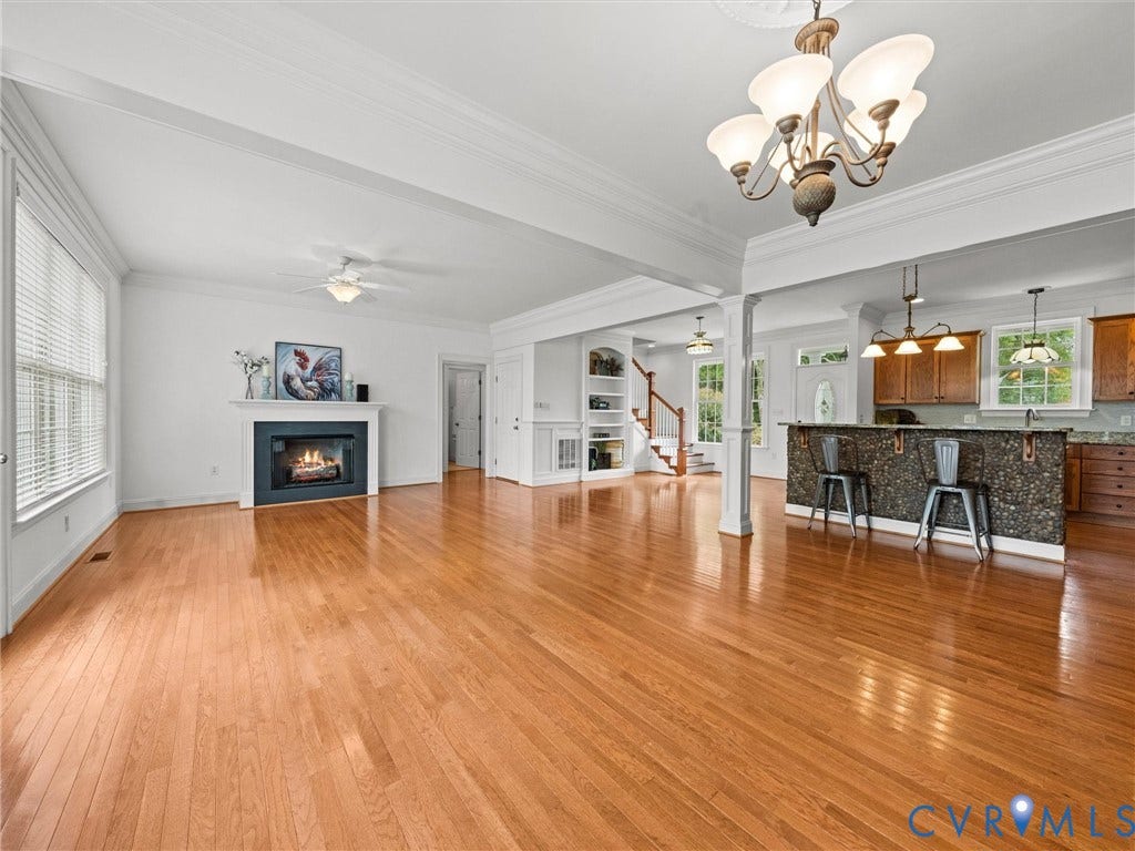 6126 Cartersville Road, Powhatan, VA 23139 Hardwood flooring throughout, a central fireplace with a white mantel, crown molding, built-in shelving, and a kitchen island with a stone facade