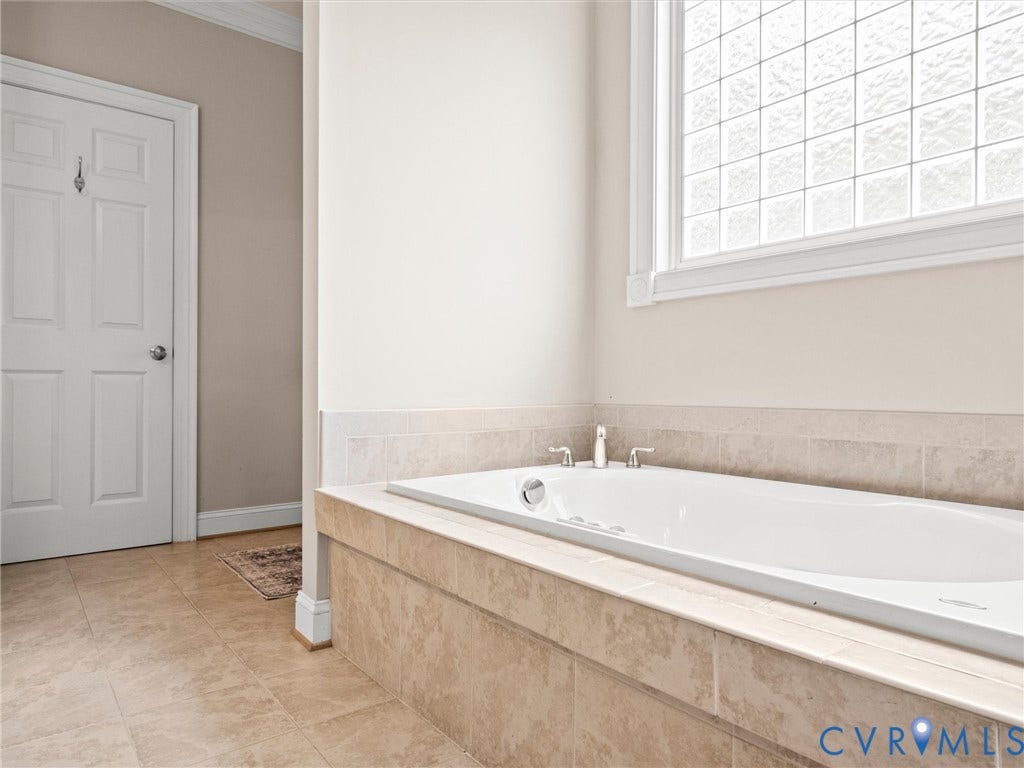 6126 Cartersville Road, Powhatan, VA 23139 Built-in soaking tub with brushed nickel fixtures, surrounded by a tiled deck and wainscoting, under a window with privacy glass blocks