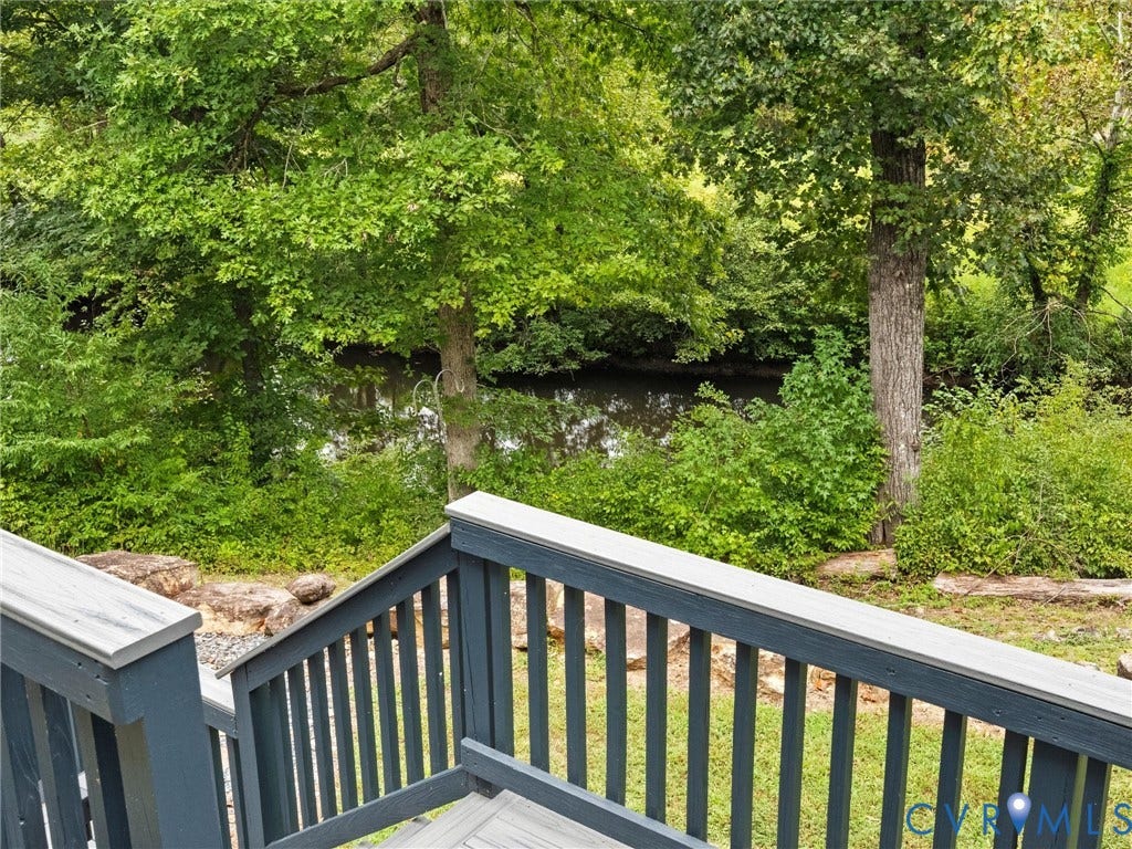 6126 Cartersville Road, Powhatan, VA 23139 Wood-finish deck with dark-stained railing overlooking a lush, wooded area and water feature