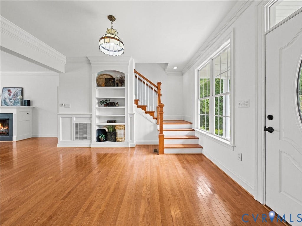 6126 Cartersville Road, Powhatan, VA 23139 Hardwood flooring, white built-in shelving, staircase with wood handrail, fireplace with white mantel, and a multi-pane window