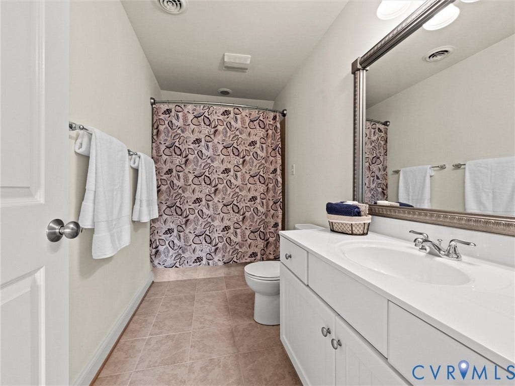 6126 Cartersville Road, Powhatan, VA 23139 Single vanity with an integrated sink and base cabinetry, complemented by a large framed mirror and a shower with a curved curtain rod