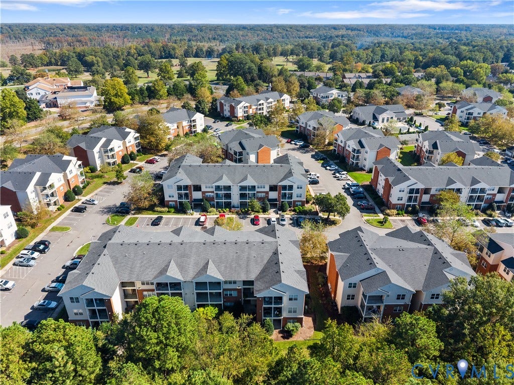 821 Brassie Lane, #E, The Crossings Golf Course Area, Glen Allen, VA 23059 Aerial perspective of a multi-building residential complex featuring shingled roofs, private balconies, paved surface parking, and extensive mature tree canopy