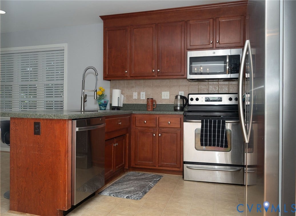 15349 Featherchase Drive, Chesterfield, VA 23832 Kitchen featuring wood cabinetry, stainless steel appliances, a tiled backsplash, and an island with a built-in sink
