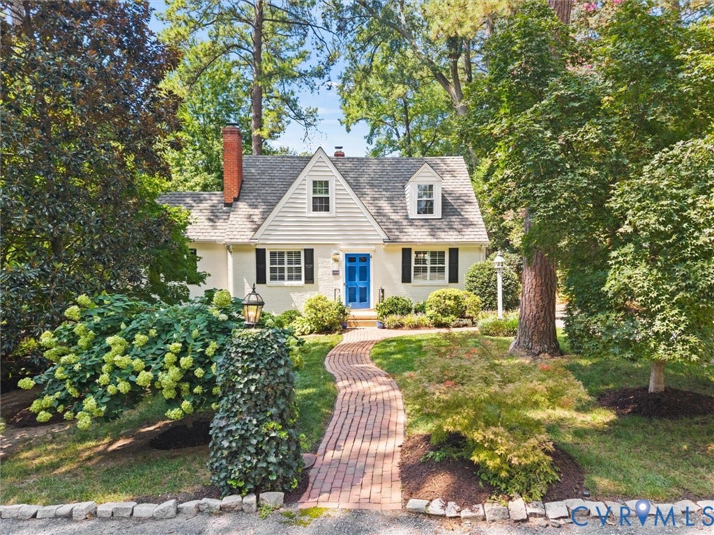 White exterior with black shutters, a blue front door, a red brick chimney, and a gray shingled roof