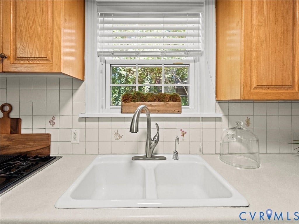 Double basin sink with a chrome faucet, light-toned countertop, and square tile backsplash